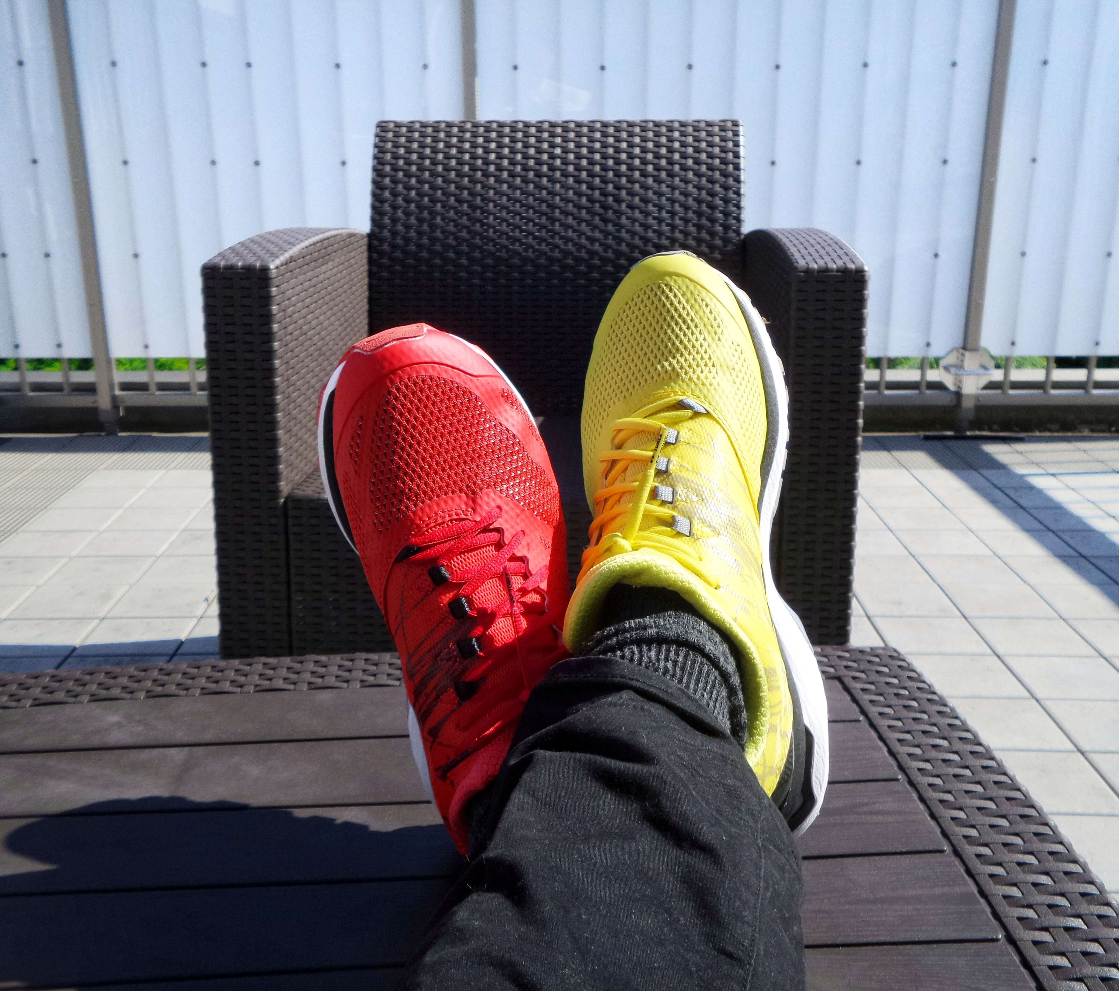 Someone is sitting and looking down at their feet that are resting on a stool and taking a photo of there sneakers, one is red and one is yellow