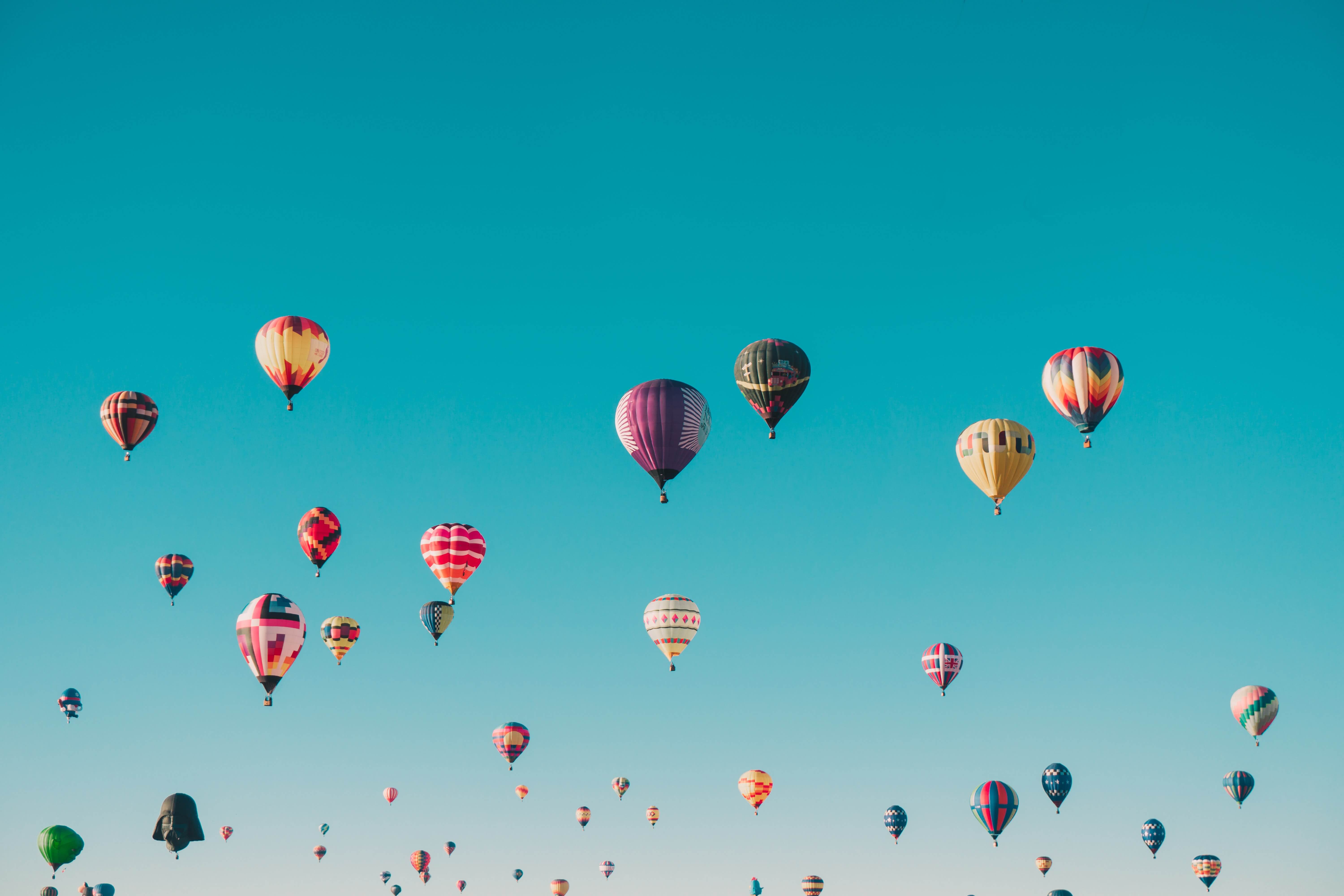 wide shot of many colourful hot air balloons flying on a clear day