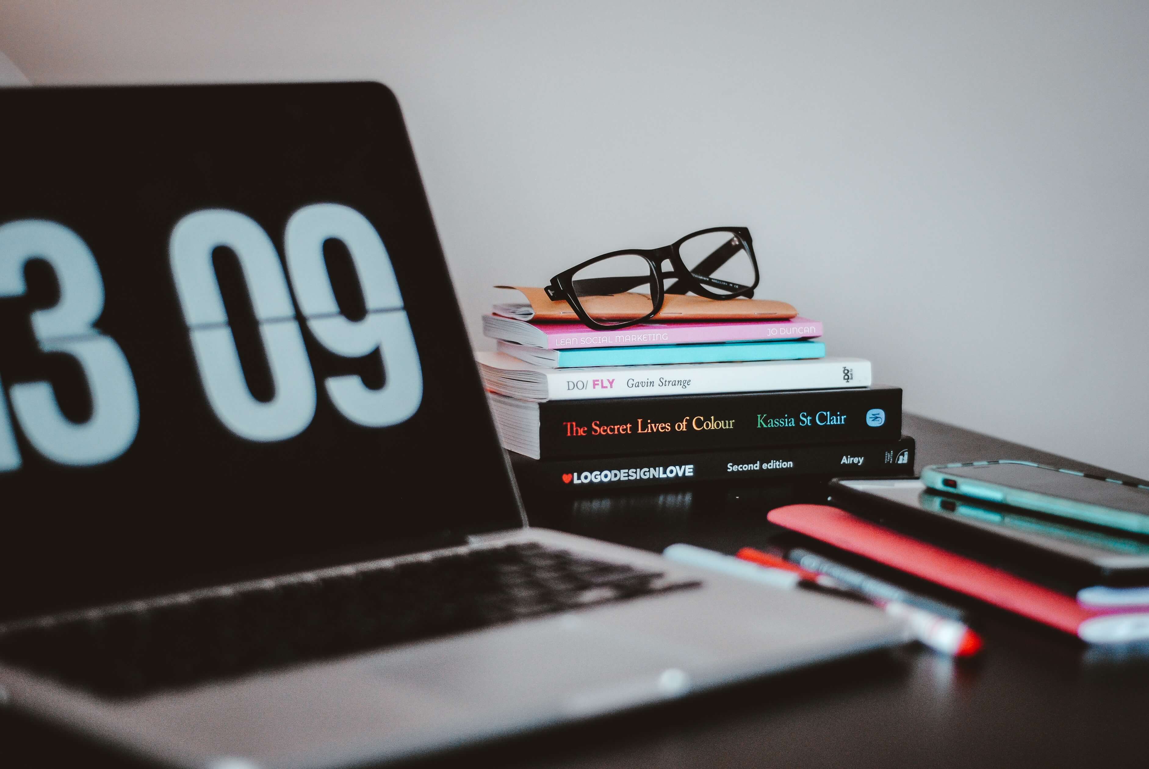 a laptop with a pair of reading glasses and a stack of design books on a desk