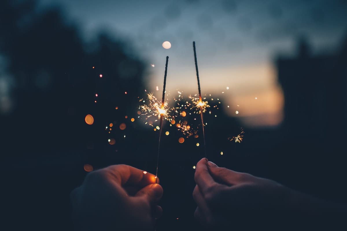 close up of two hands holding sparklers at night time