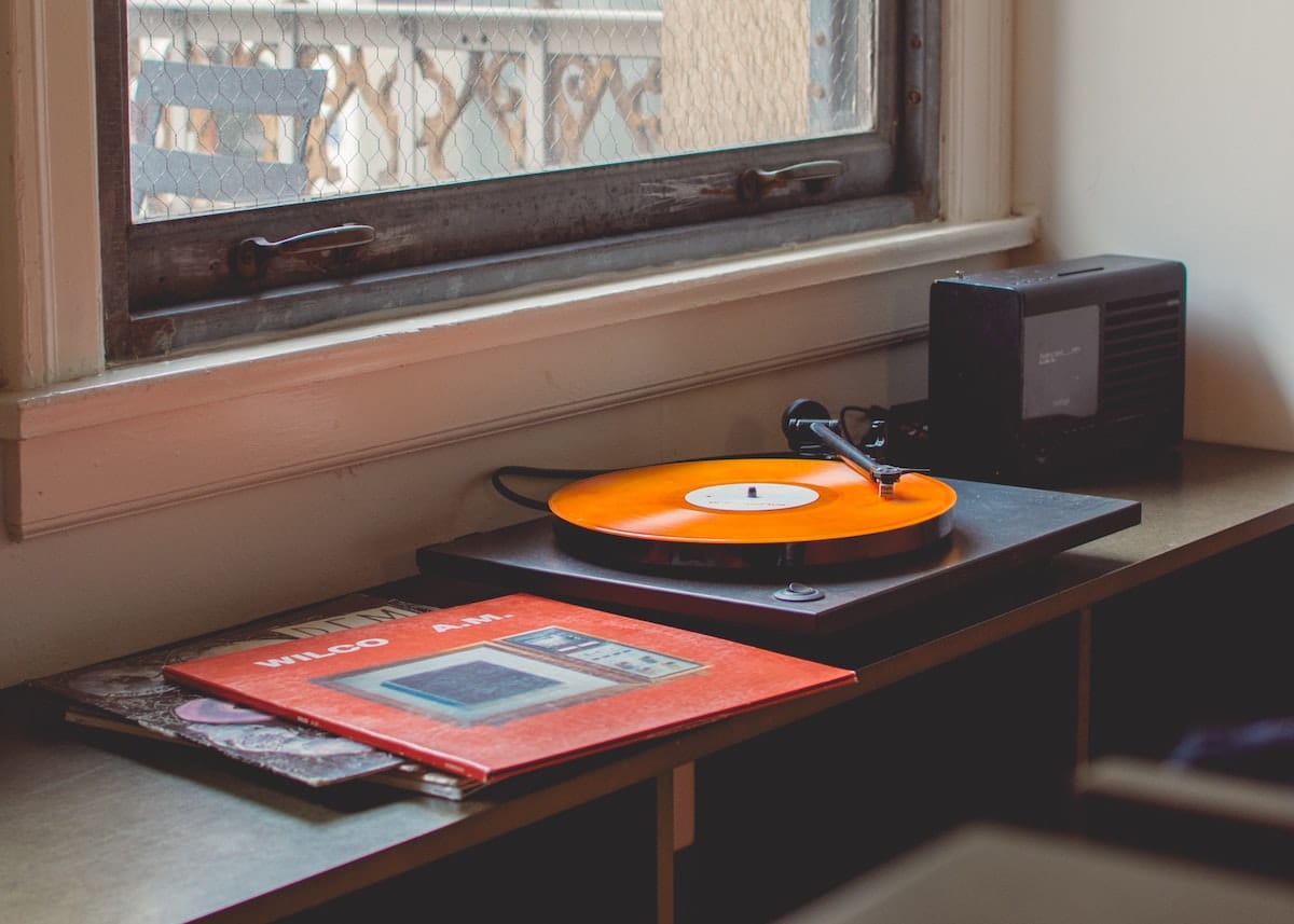 record player playing an album, beside it, a speaker and a small stack of vinyl records