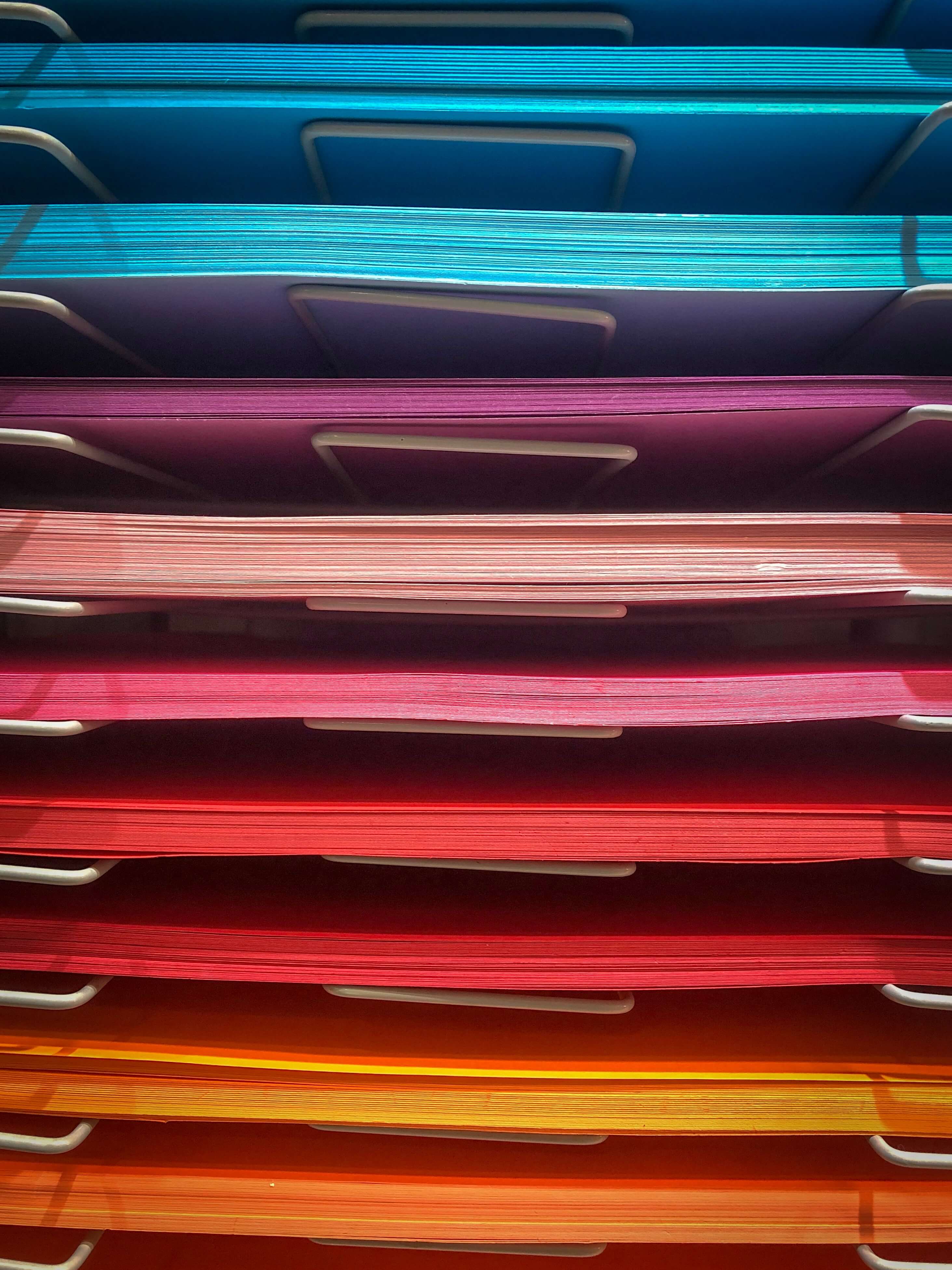 A paper shelf with coloured paper going from blue at the top to orange at the bottom.