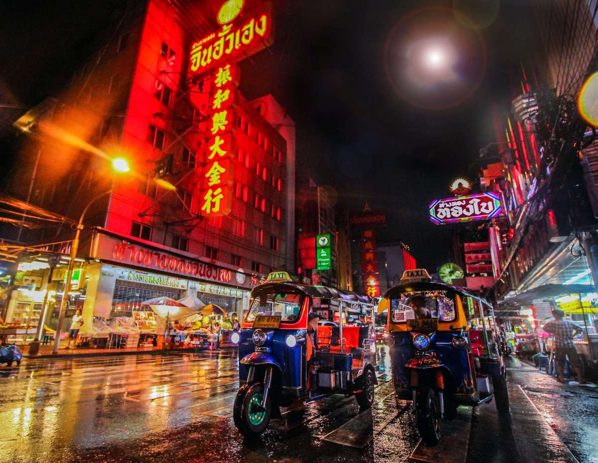 Thailand night street with bright neon lights and roaming tuk tuks