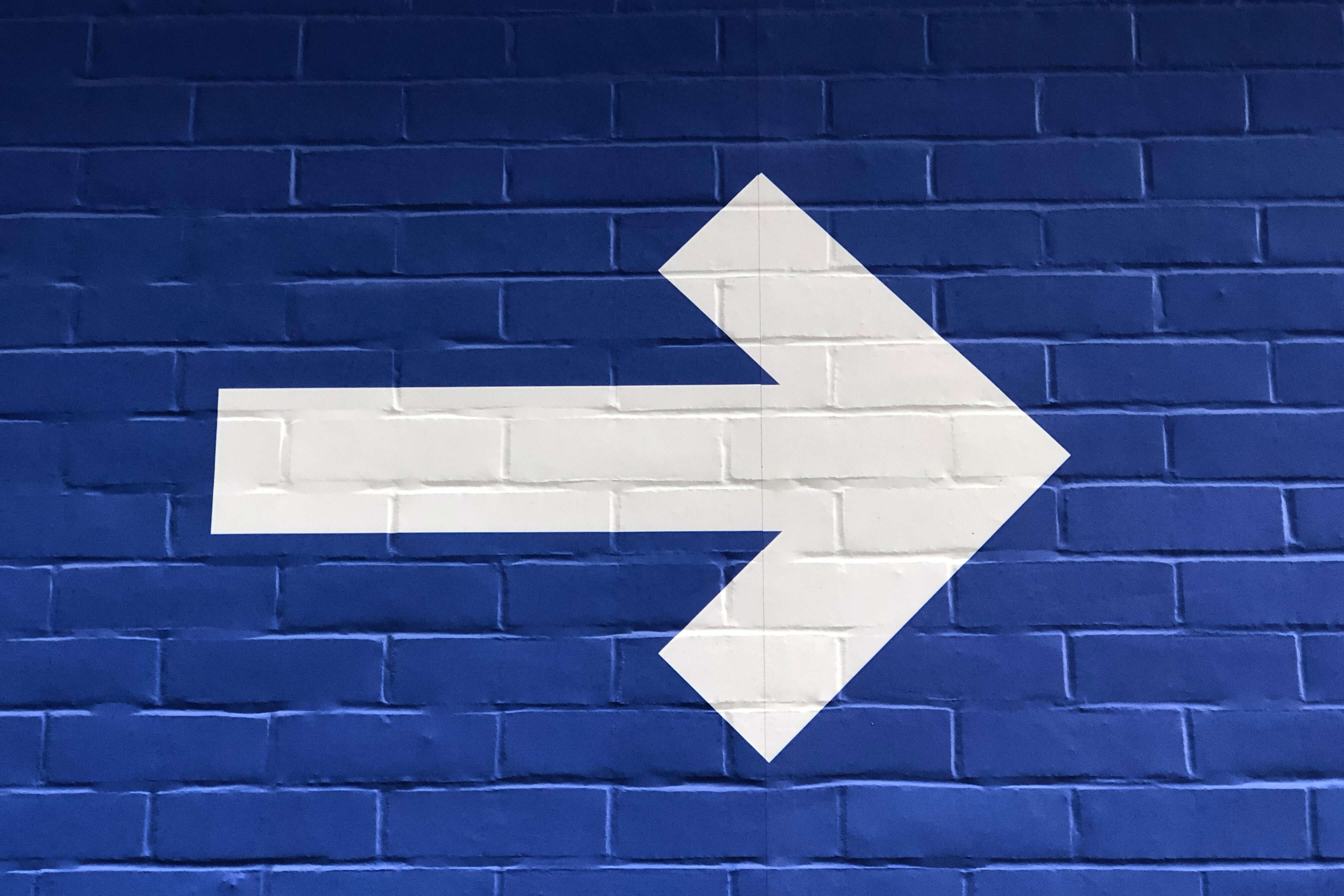 giant white arrow point to the right painted on a navy blue brick wall